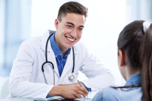 Close up portrait of young handsome medical doctor writing prescription to female patient in clinic.